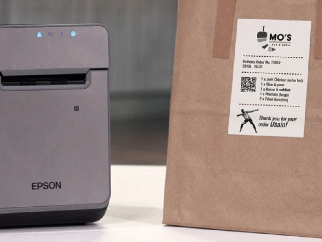 Impresora de etiquetas Epson TM-L100 junto a una bolsa de take away con la etiqueta del pedido pegada